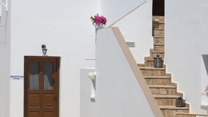 A white building with a wooden door labeled "RECEPTION," a staircase with stone steps, and a small balcony with a wooden railing. - Letta's Apartments (Syros)
