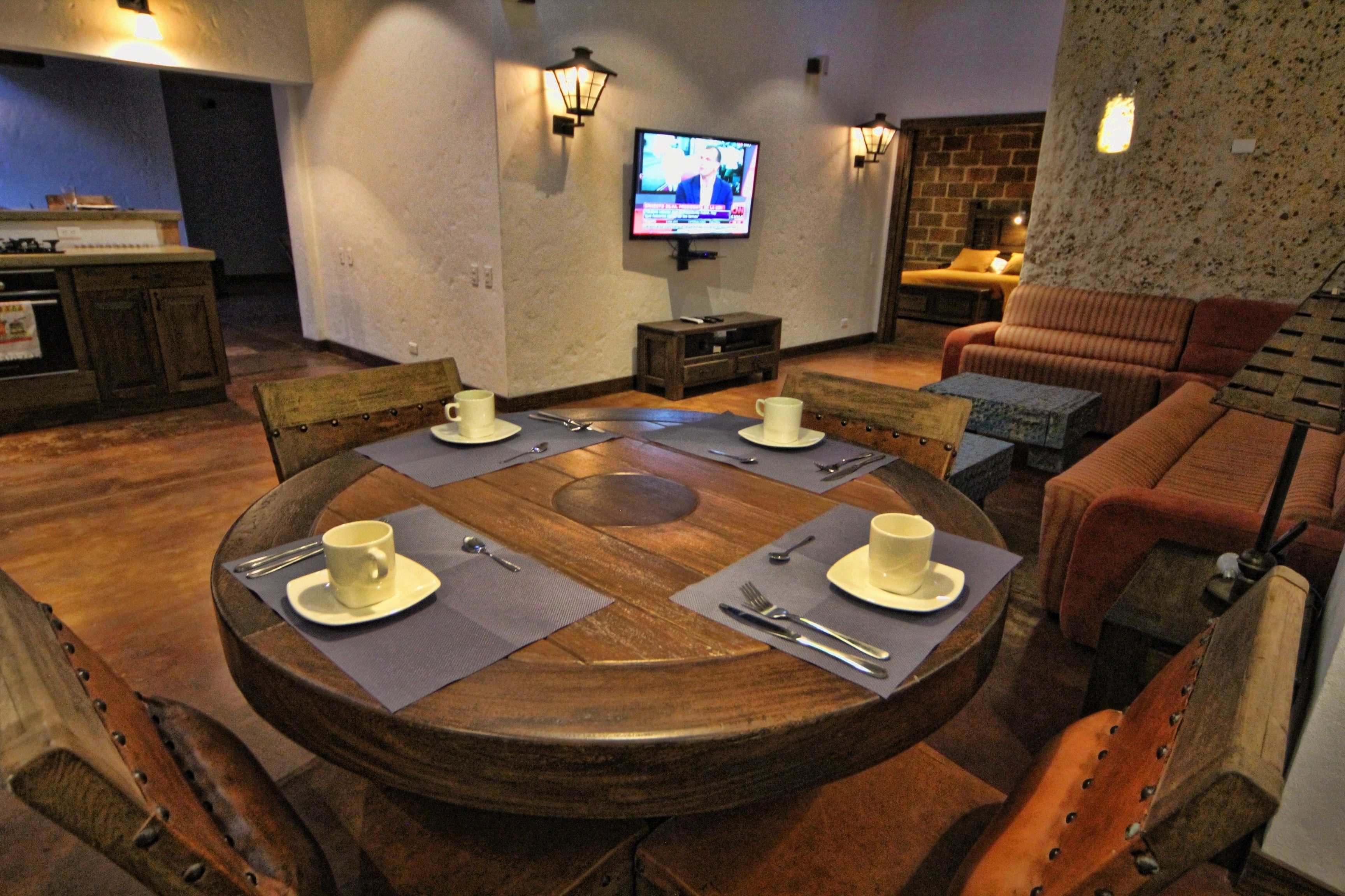 Comedor con una mesa redonda de madera dispuesta para seis personas, con tazas y cubiertos blancos.