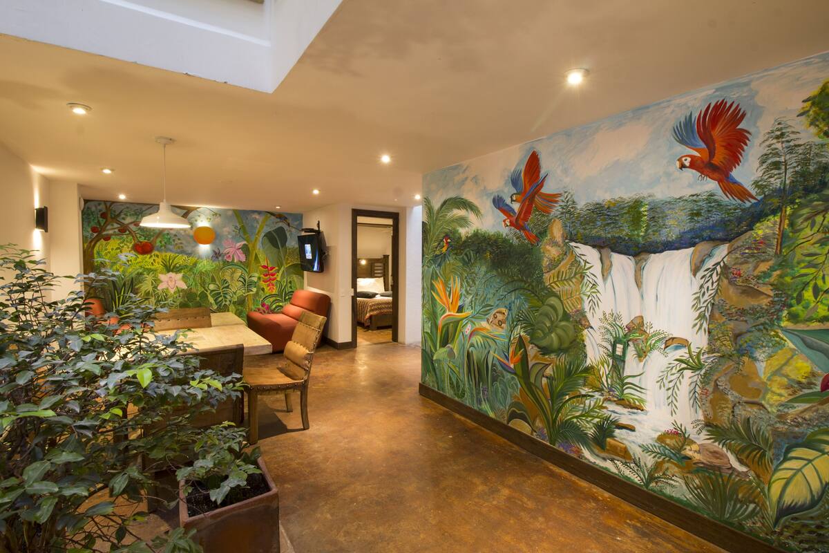 A room with a mural of a waterfall and birds, a wooden bench, and potted plants.