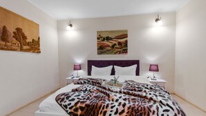 Une chambre à coucher avec un grand lit, deux tables de chevet avec des lampes, une tête de lit et deux lampes fixées au mur.
