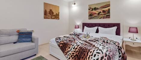 Un dormitorio con una cama, un sofá gris, una alfombra colorida y dos lámparas de pared.