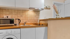 Une cuisine moderne avec des meubles blancs, un lave-linge, un four à micro-ondes et une machine à café.