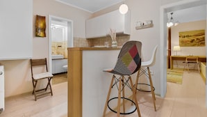 Une cuisine moderne avec un îlot central en bois, des tabourets de bar blancs et un coin repas comprenant une table et des chaises.
