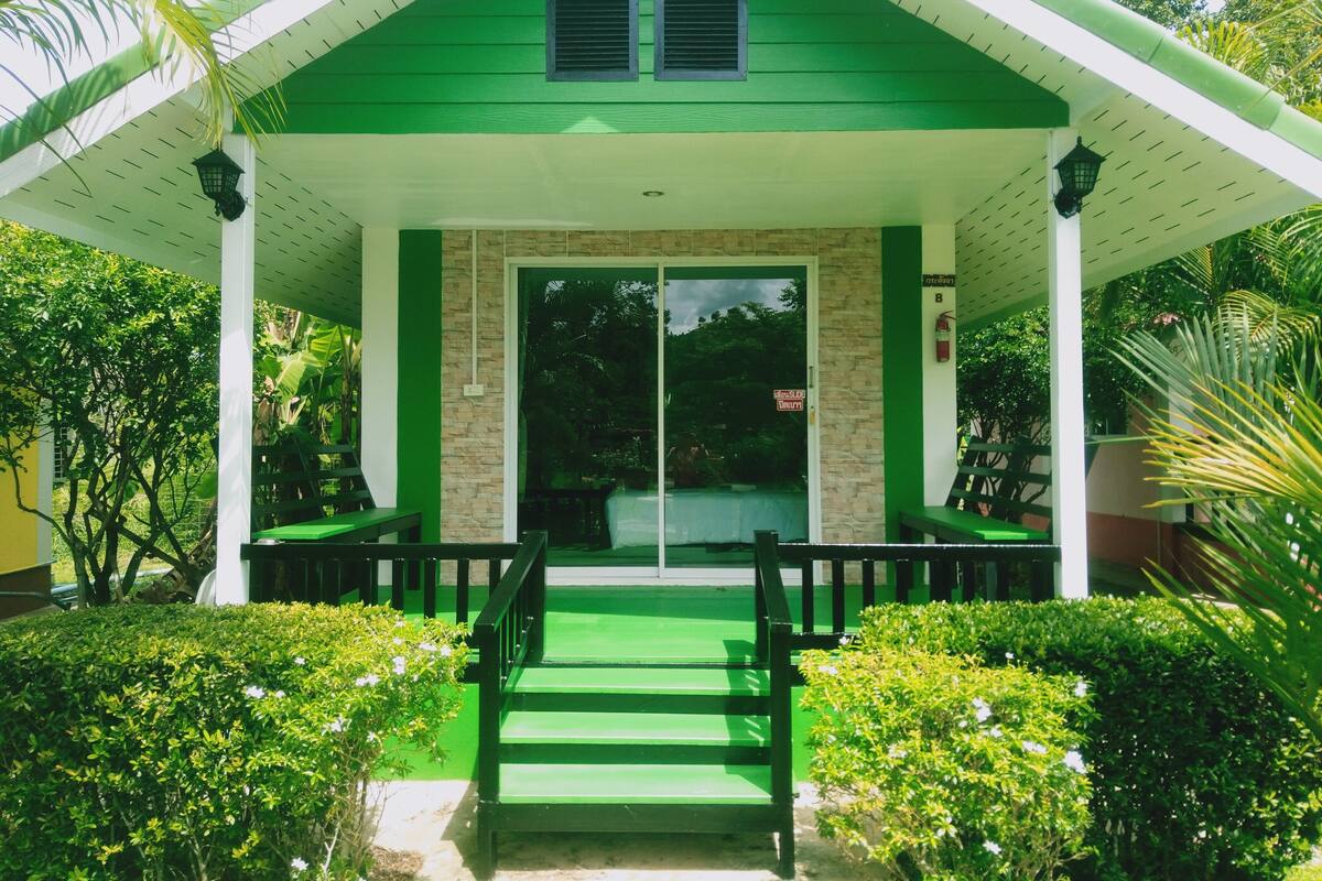 A green building with a covered entrance, steps leading up to it, and a sign indicating a fire exit.