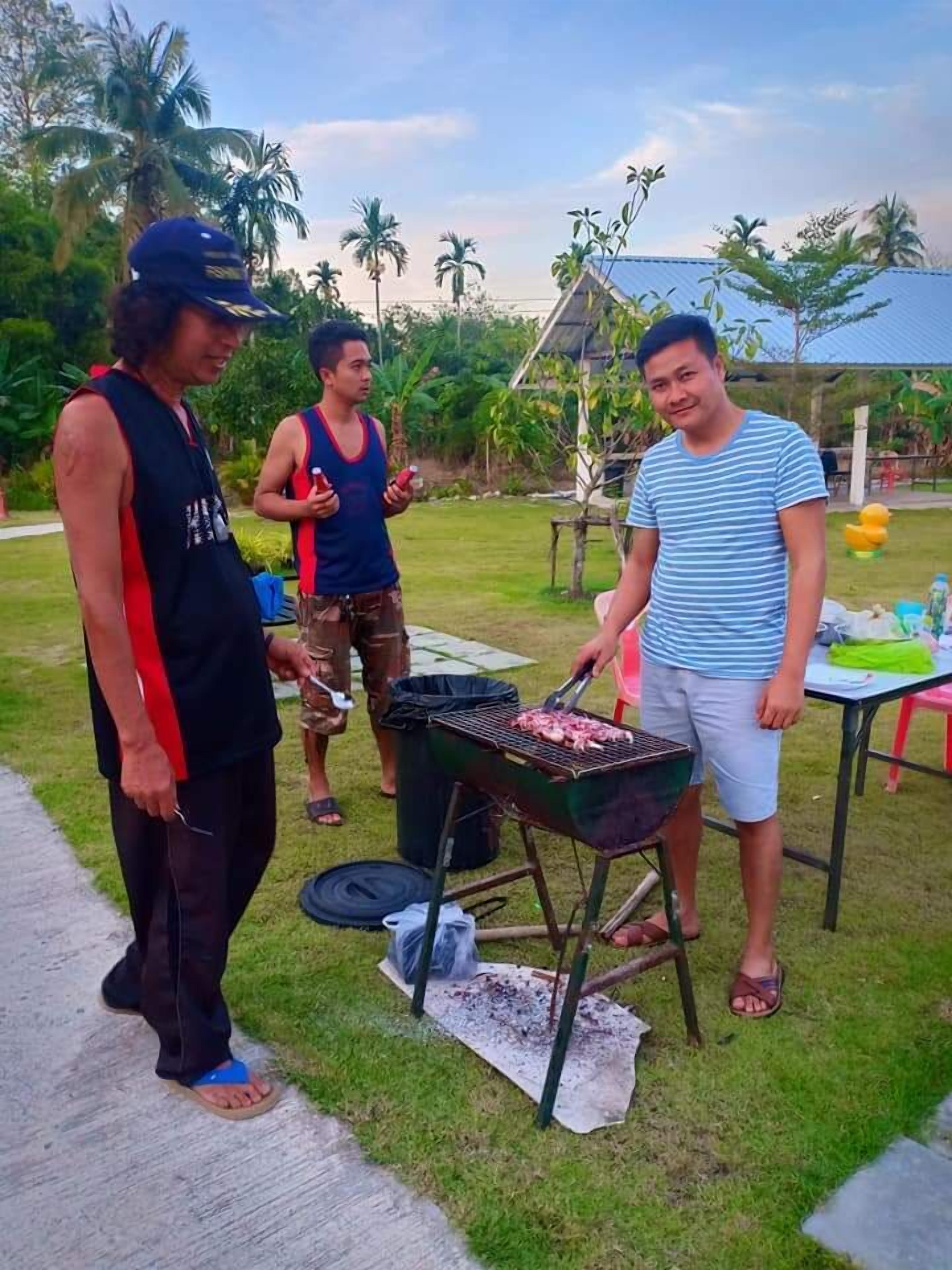 A group of people grilling outdoors with a portable grill and a table with items on it.