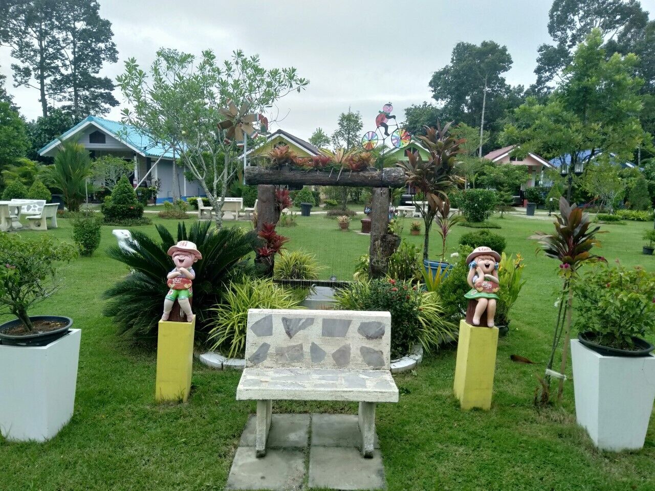 A garden with a stone bench, two decorative figures, and a small bridge.