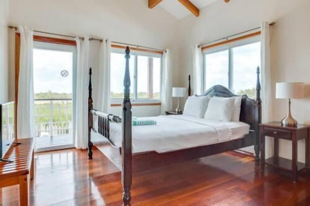 Un dormitorio espacioso con una cama grande, piso de madera y varias ventanas con vistas.