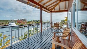 Una terraza techada al aire libre con sillas y mesas de madera, con vista a un puerto deportivo con barcos y edificios.