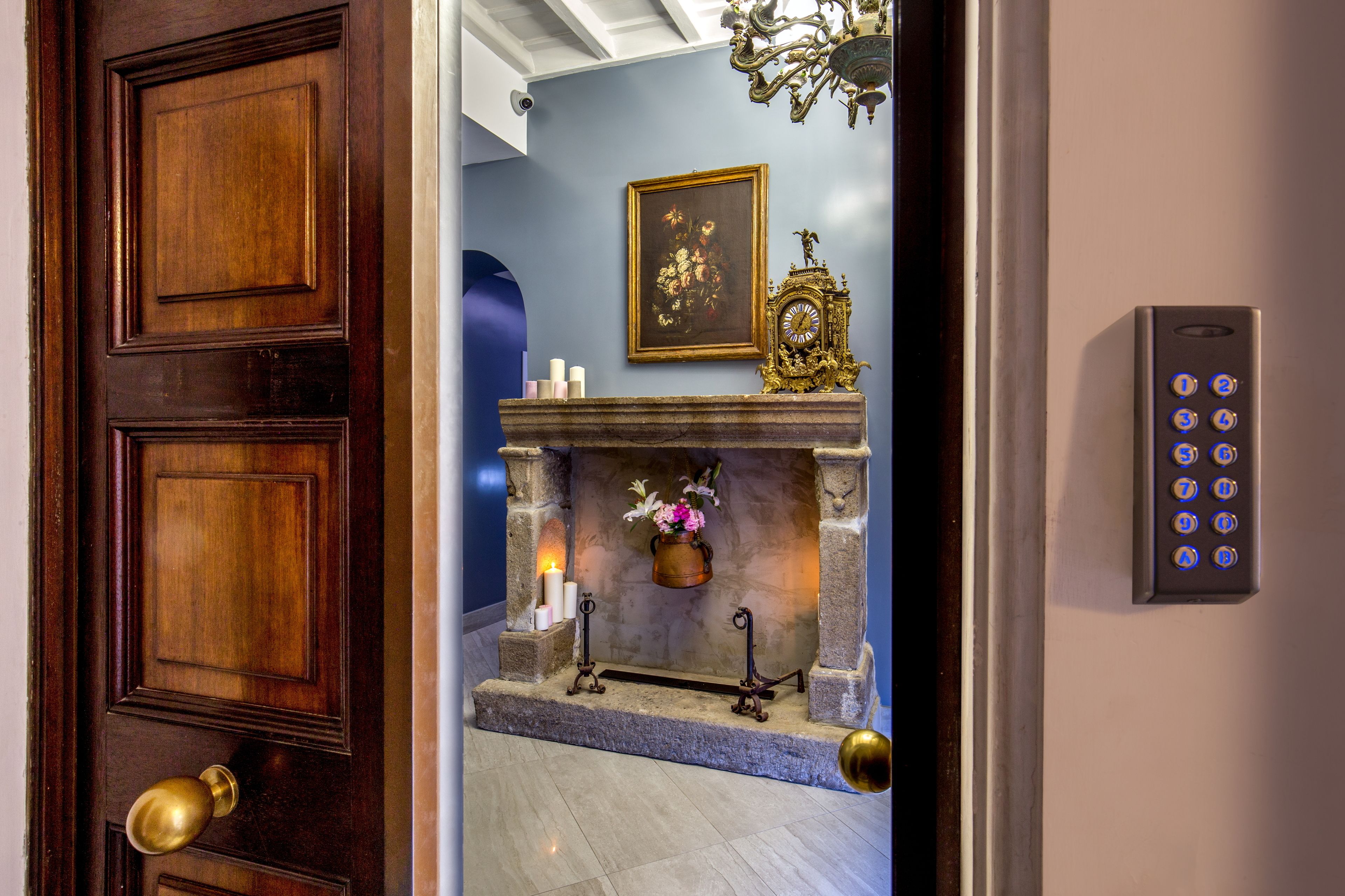 A wooden door with a brass doorknob, a stone fireplace with a vase of flowers, a framed painting, and a wall-mounted elevator control panel.