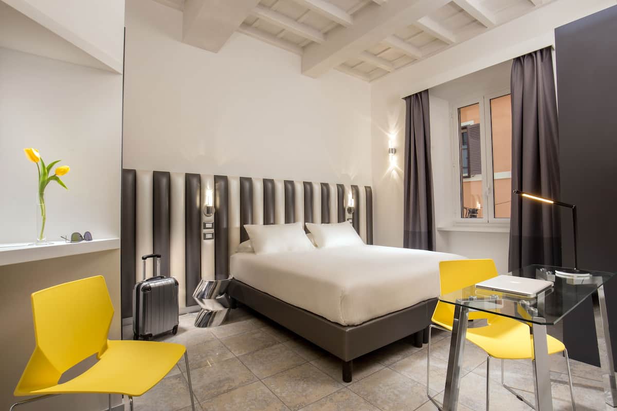 Et moderne hotelværelse med en stor seng, to gule stole, et lille bord og en kuffert.