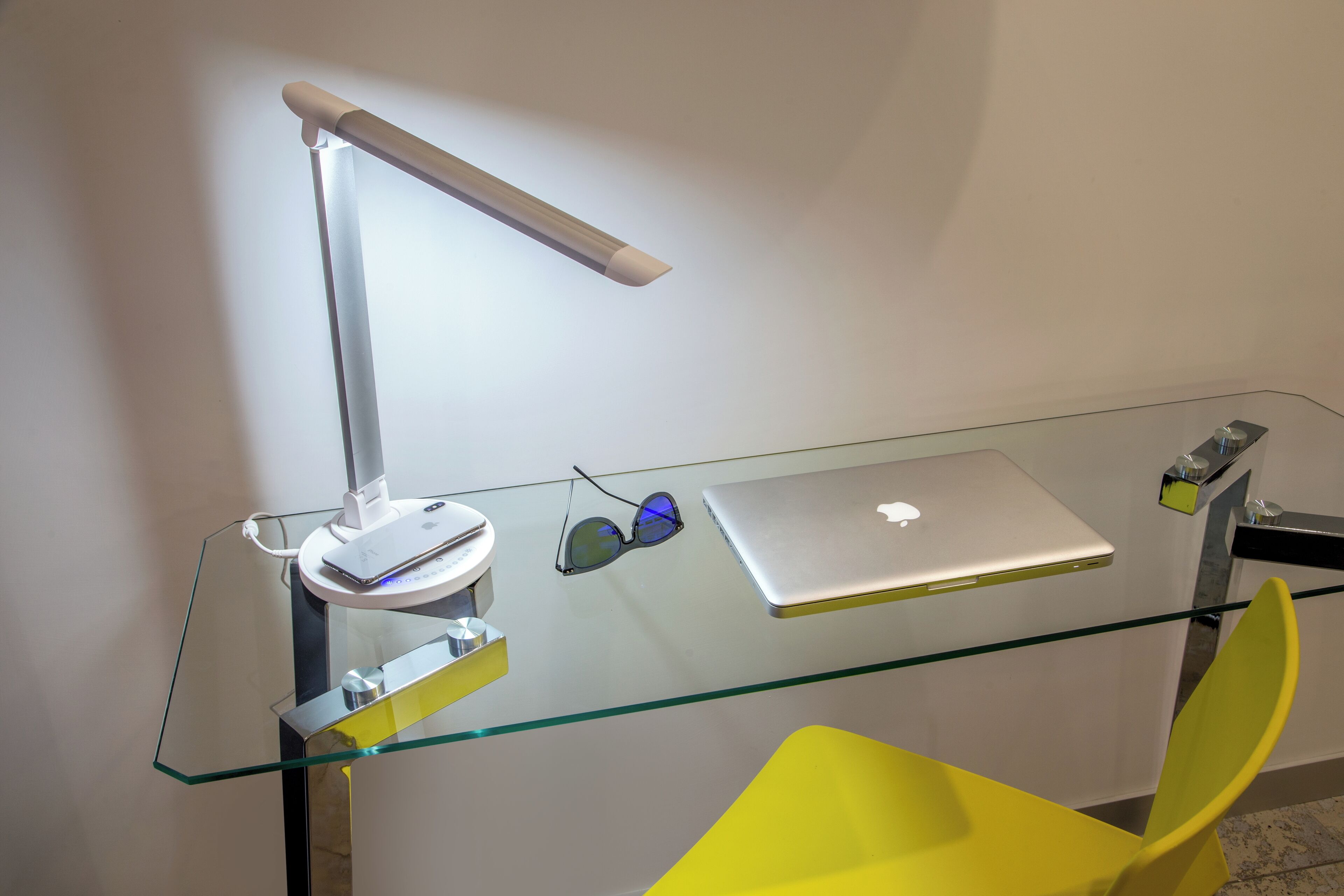 A modern workspace with a glass desk, a laptop, a desk lamp, and a pair of headphones.