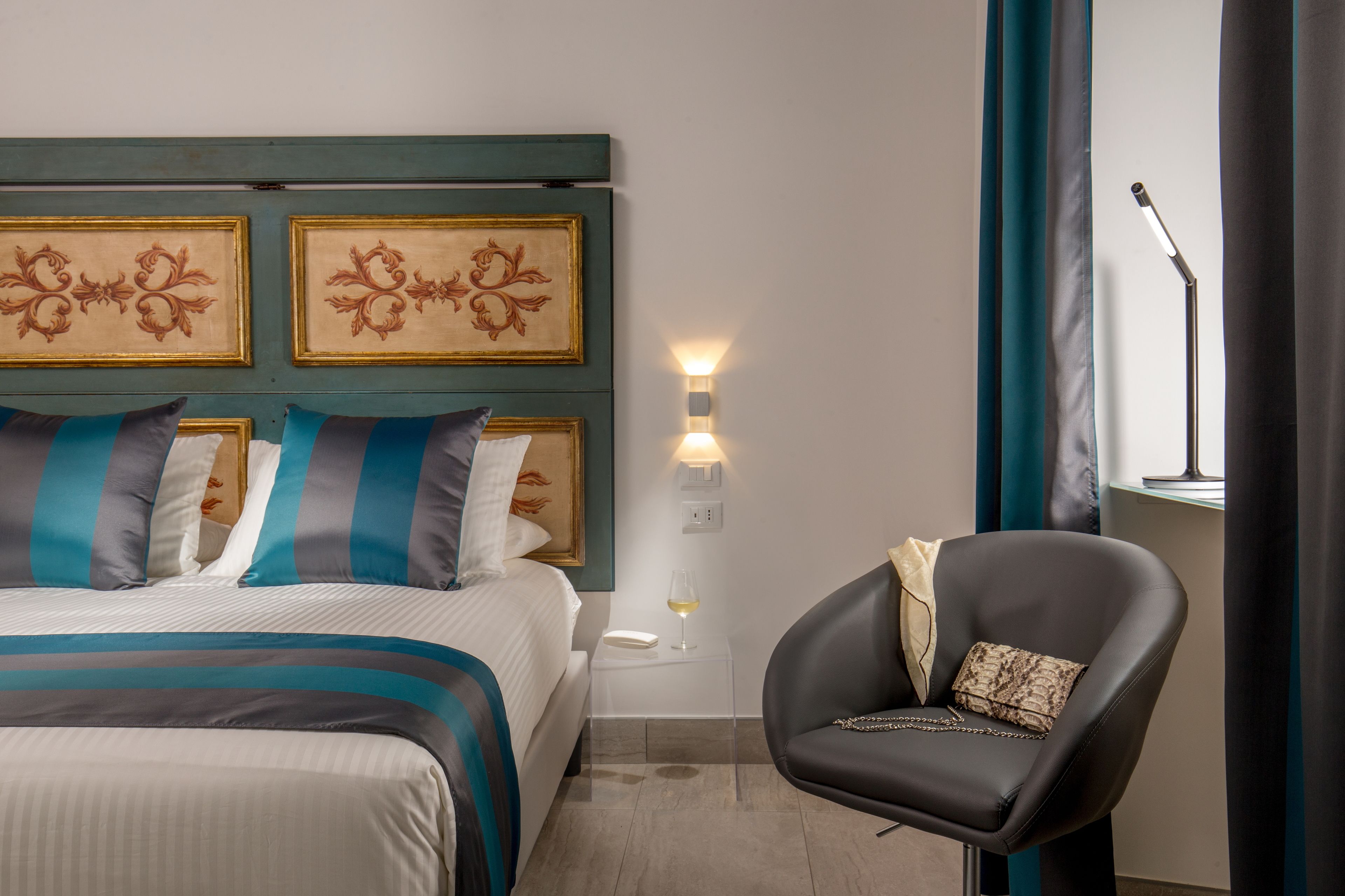 Una habitación de hotel con una cama, una silla, una mesita de noche y una lámpara fijada a la pared.
