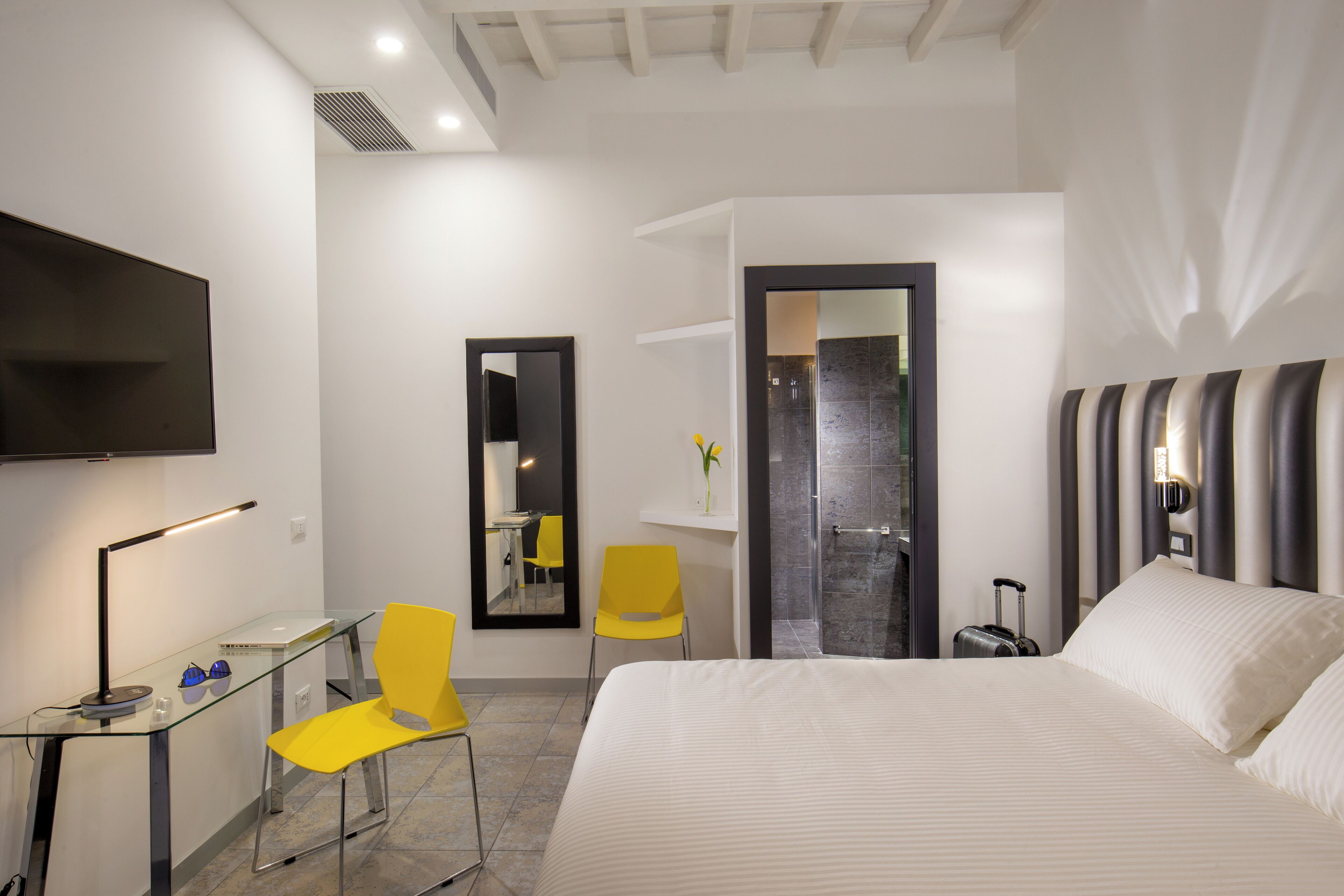A hotel room with a bed, a desk with a chair, a TV, and a shower area.
