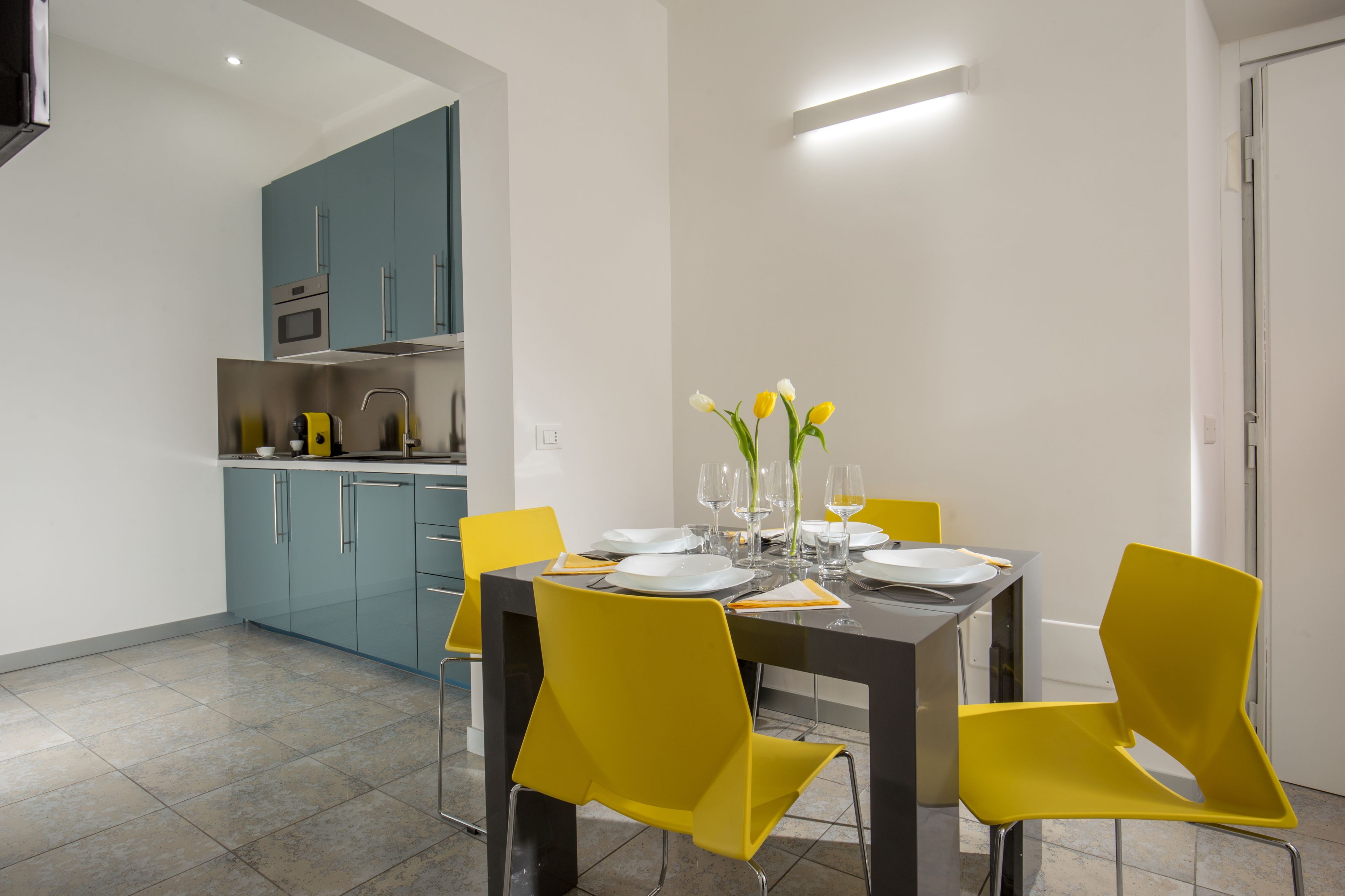 A modern dining area with a table set for four, yellow chairs, and a vase with flowers.