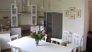 Une cuisine moderne avec des meubles blancs, un réfrigérateur en acier inoxydable et une table à manger avec des chaises.