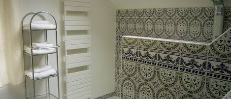 Un baño con un perchero metálico, un estante blanco para toallas, azulejos estampados y un tragaluz.