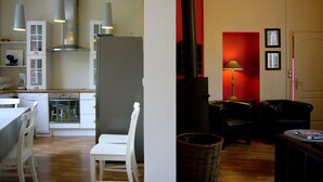 Une cuisine moderne avec des meubles blancs, un coin repas avec une table et des chaises blanches, et un salon doté d’une cheminée et de canapés en cuir.