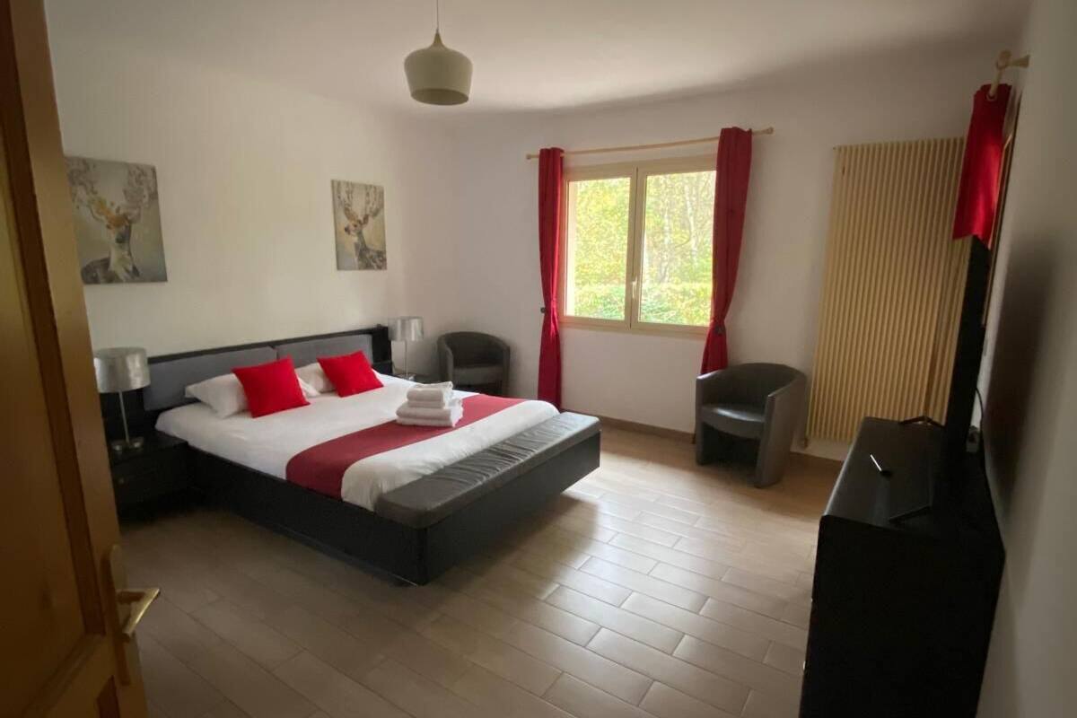 A bedroom with a bed, a chair, a desk, a window with curtains, and artwork on the walls.