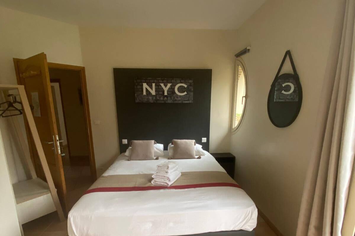A hotel room with a bed, a wall-mounted mirror, a door, and a tiled floor.