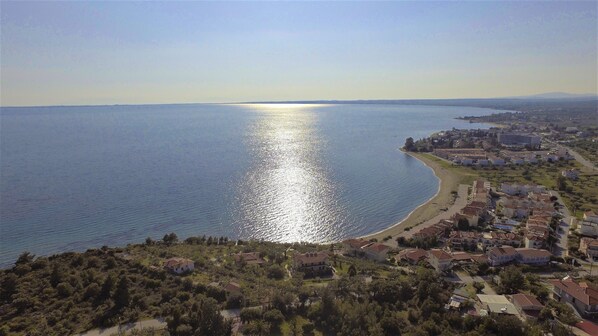 Un pueblo costero con playa, casas y una extensa masa de agua reflejando la luz del sol.