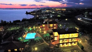 An aerial view of a coastal property at dusk with a swimming pool, multiple buildings, and a view of the sea. - Sunday Summer Resort (Polygyros)