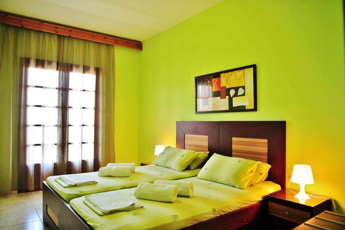 A hotel room with a large bed, two bedside tables, a nightstand, and a window with curtains.