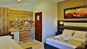 A compact hotel room with a kitchenette, a bed with neatly made linens, and a painting on the wall. - Sunday Summer Resort (Polygyros)