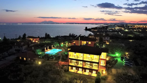 A multi-story hotel with a pool, surrounded by trees and a view of the sea at dusk. - Sunday Summer Resort (Polygyros)