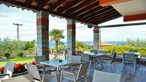 An outdoor patio with tables and chairs, stone pillars, and a view of the sea. - Sunday Summer Resort (Polygyros)