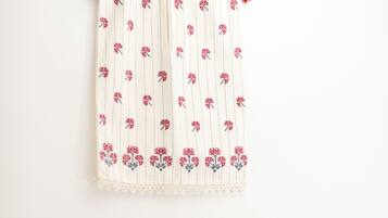 A white wall with a hanging curtain featuring a floral pattern. Below the curtain, there is a wooden nightstand with a white lamp and a power outlet.
