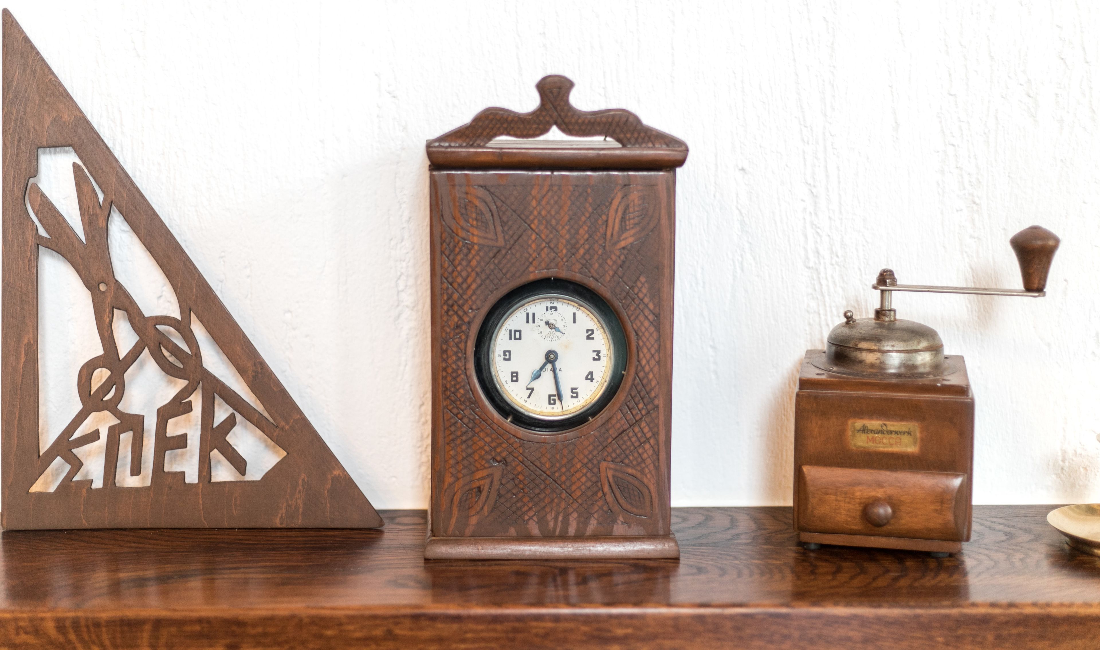 Un reloj de madera con un marco triangular, una esfera redonda y un pequeño mecanismo a su lado.