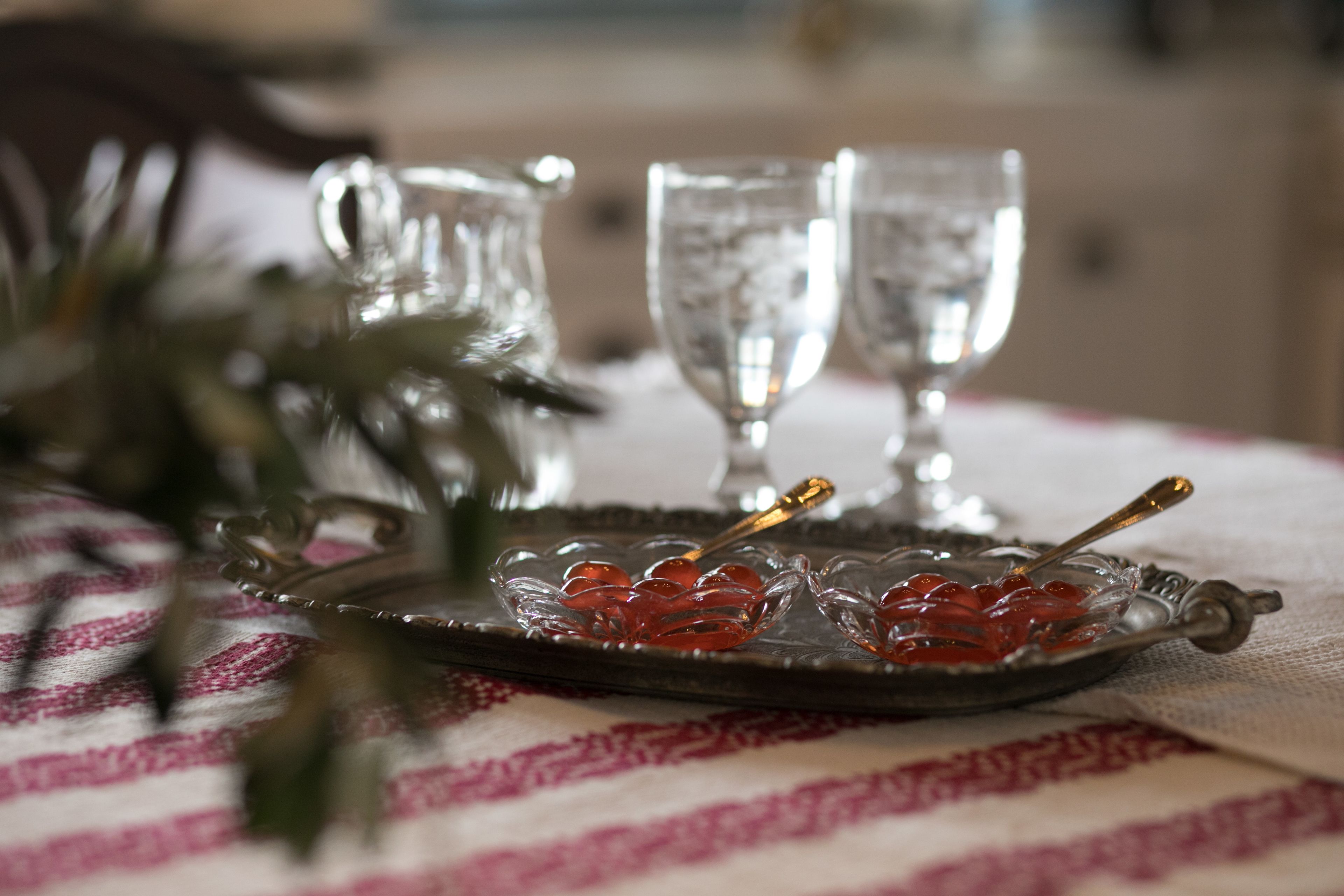 A tray with red candies and a spoon on a tablecloth.
