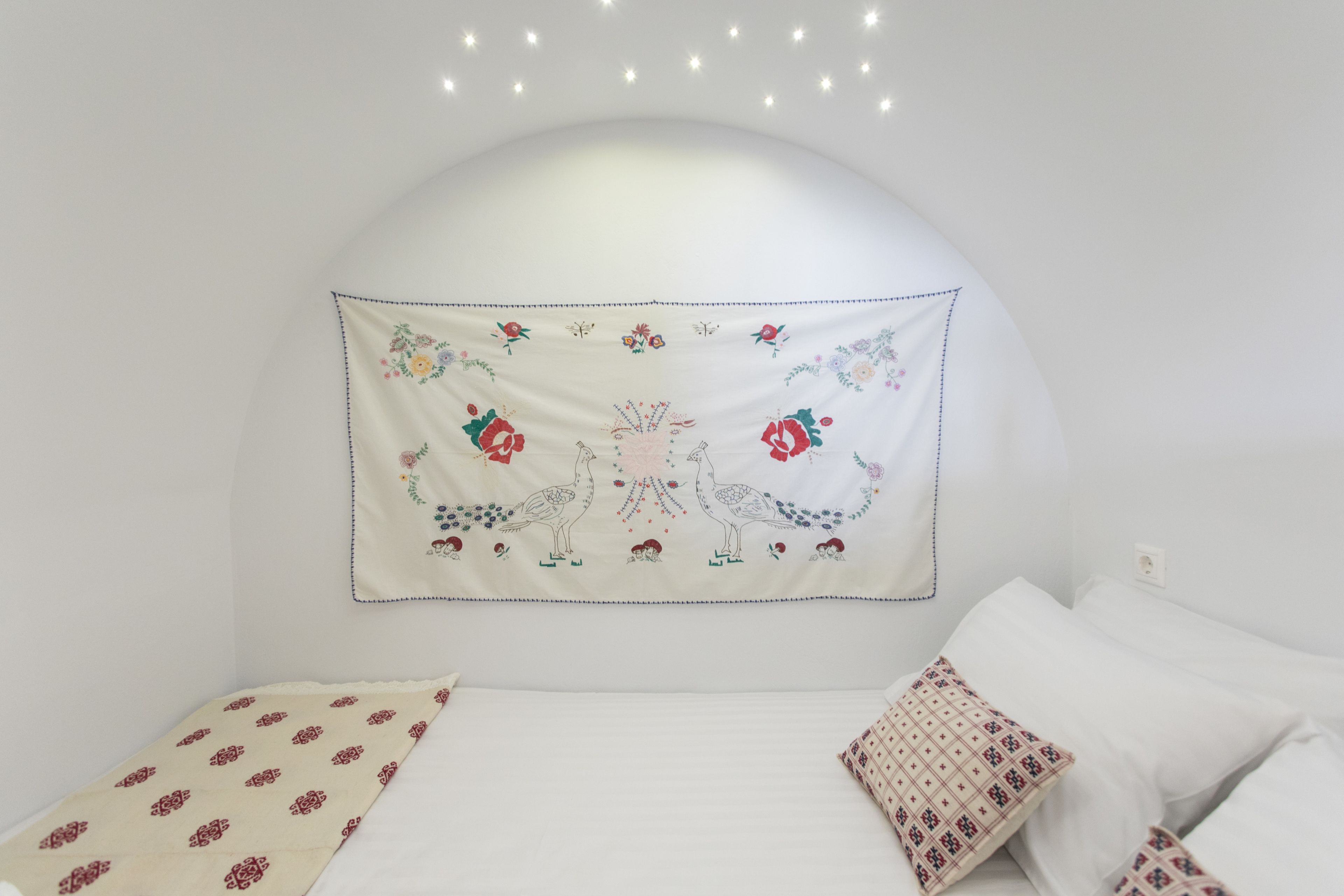 A bedroom with a white headboard, a bed with white bedding, and a decorative tapestry with floral and animal designs.