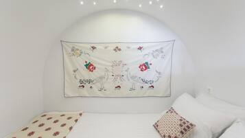 A bedroom with a white headboard, a bed with white bedding, and a decorative tapestry with floral and animal designs.