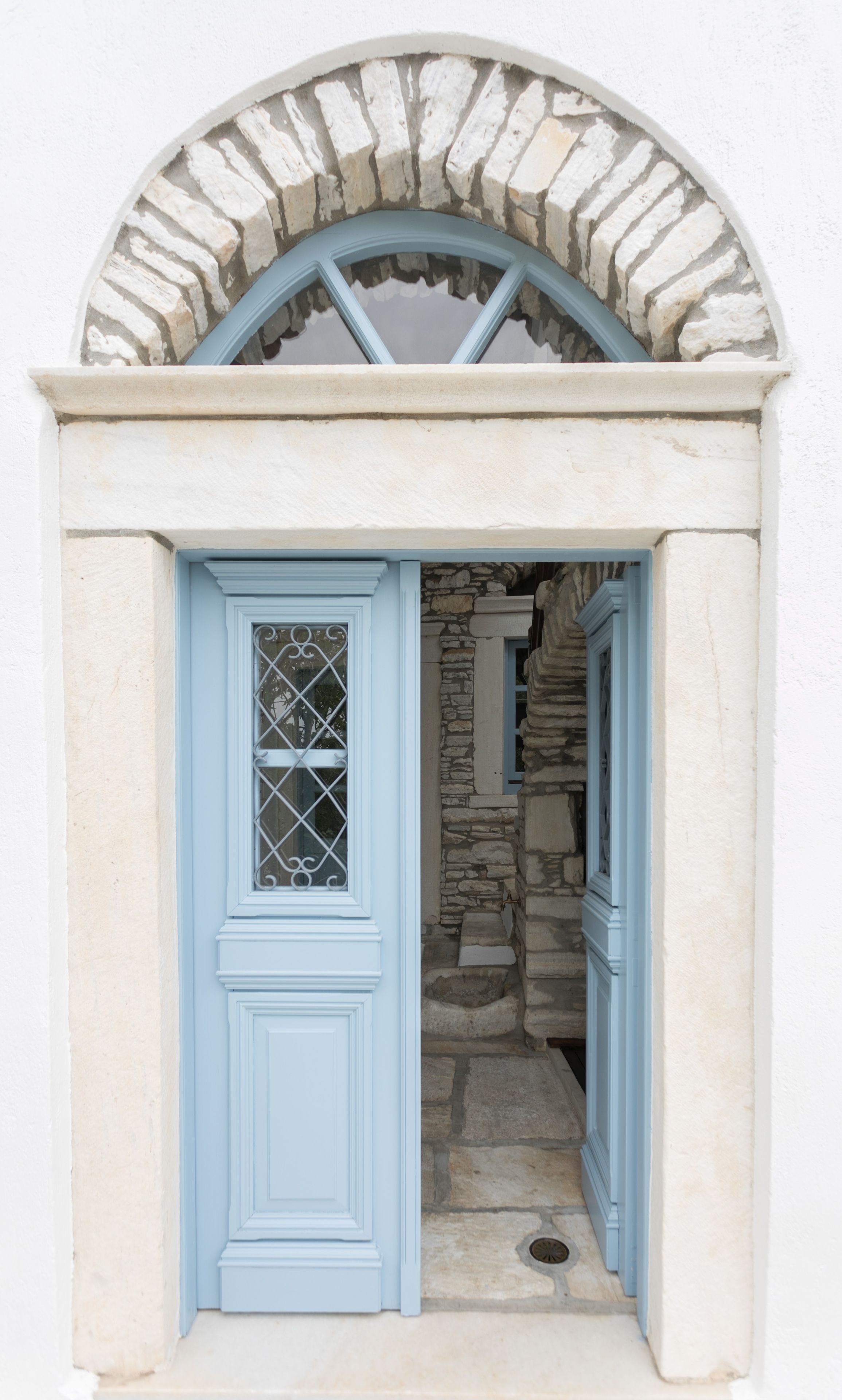 Un vano con arco de piedra y una puerta azul con un panel de vidrio decorativo.