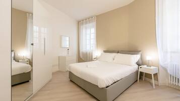 A modern bedroom with a large bed, bedside tables, a mirror, and a window with sheer curtains.