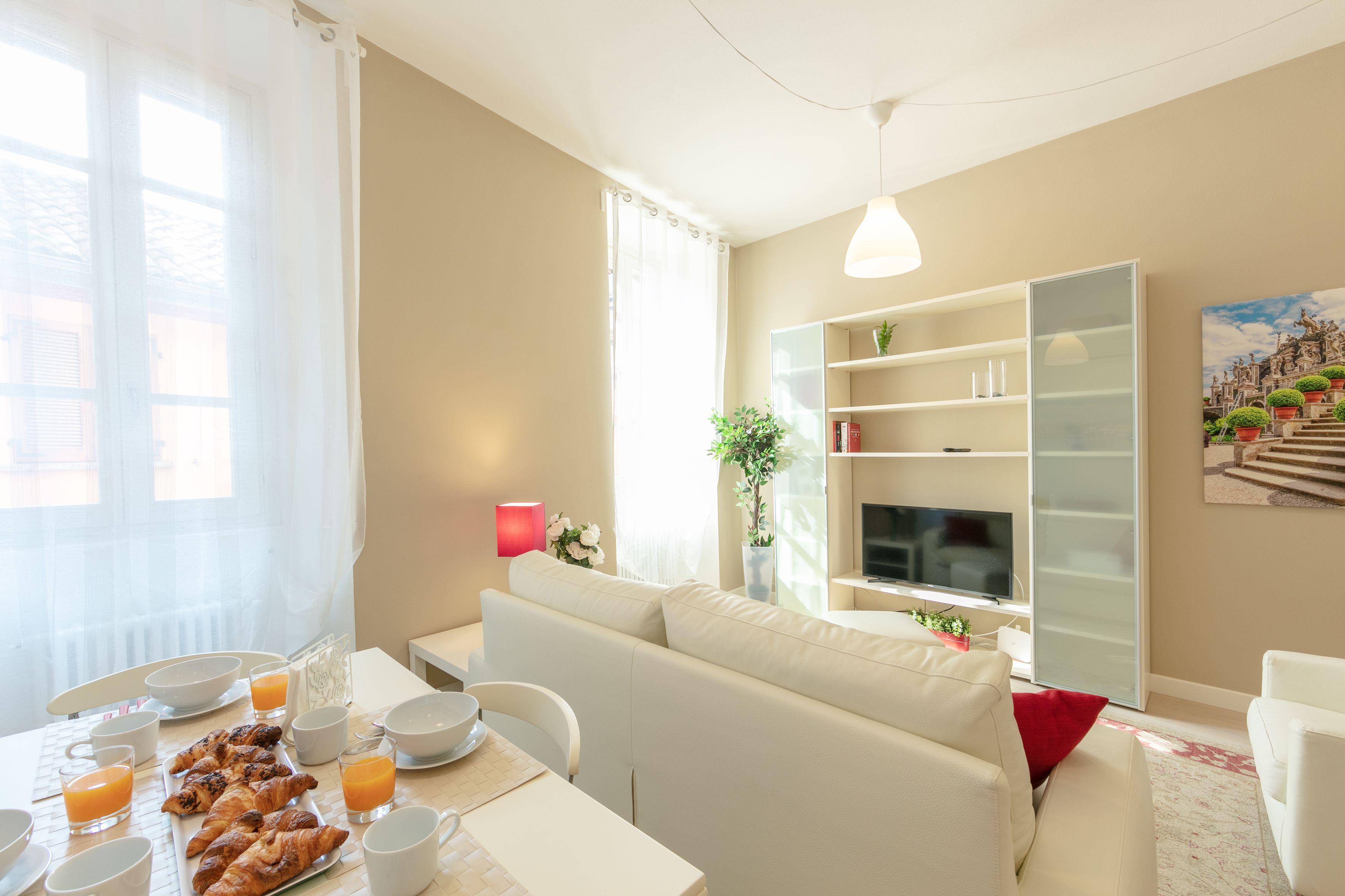 A modern living room with a sofa, a dining table with breakfast items, a TV, and a bookshelf.