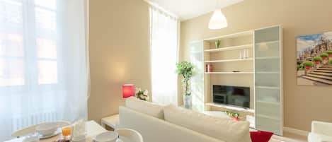 A modern living room with a sofa, a dining table with breakfast items, a TV, and a bookshelf.