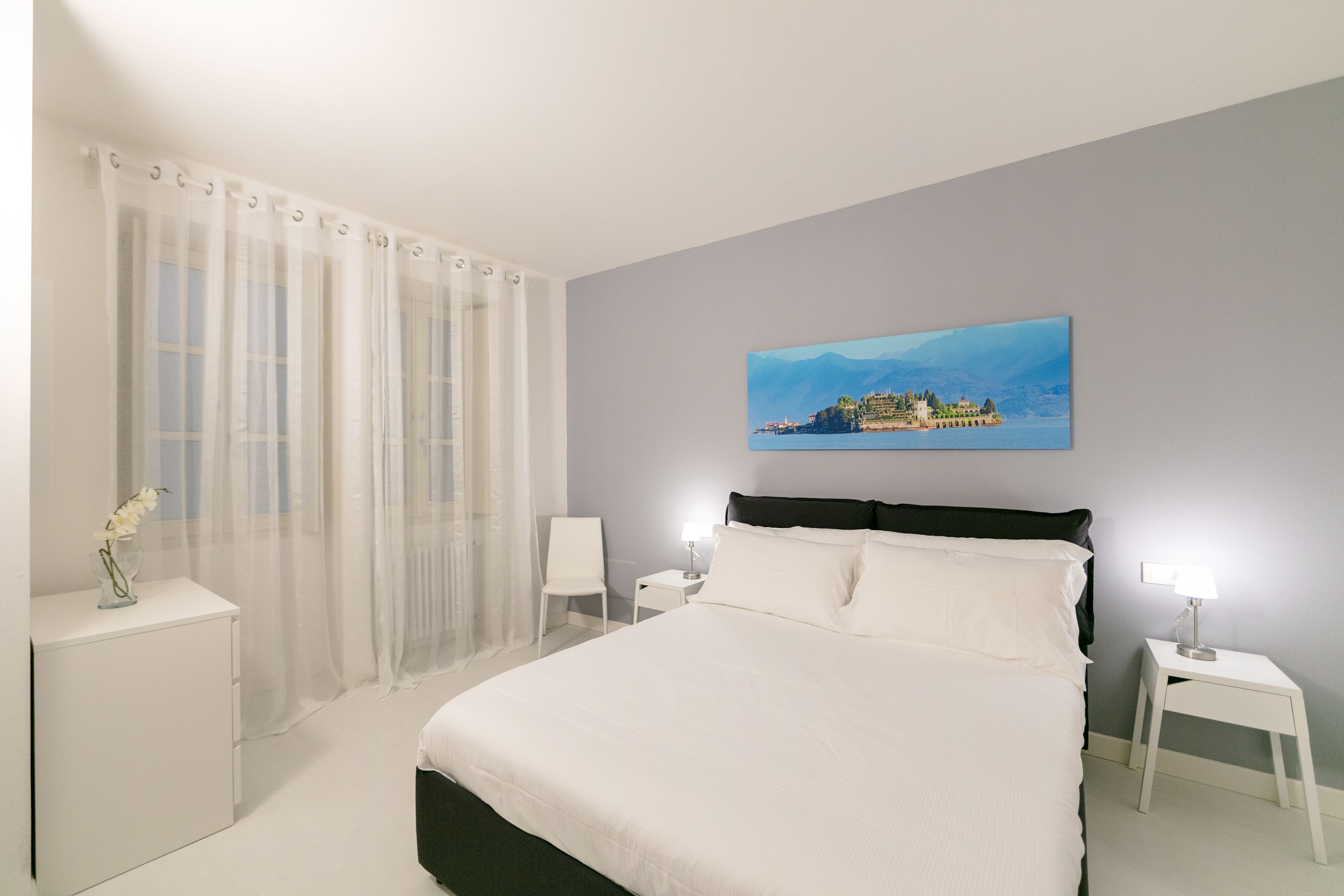 A bedroom with a bed, a nightstand, a chair, a desk, and a painting on the wall.