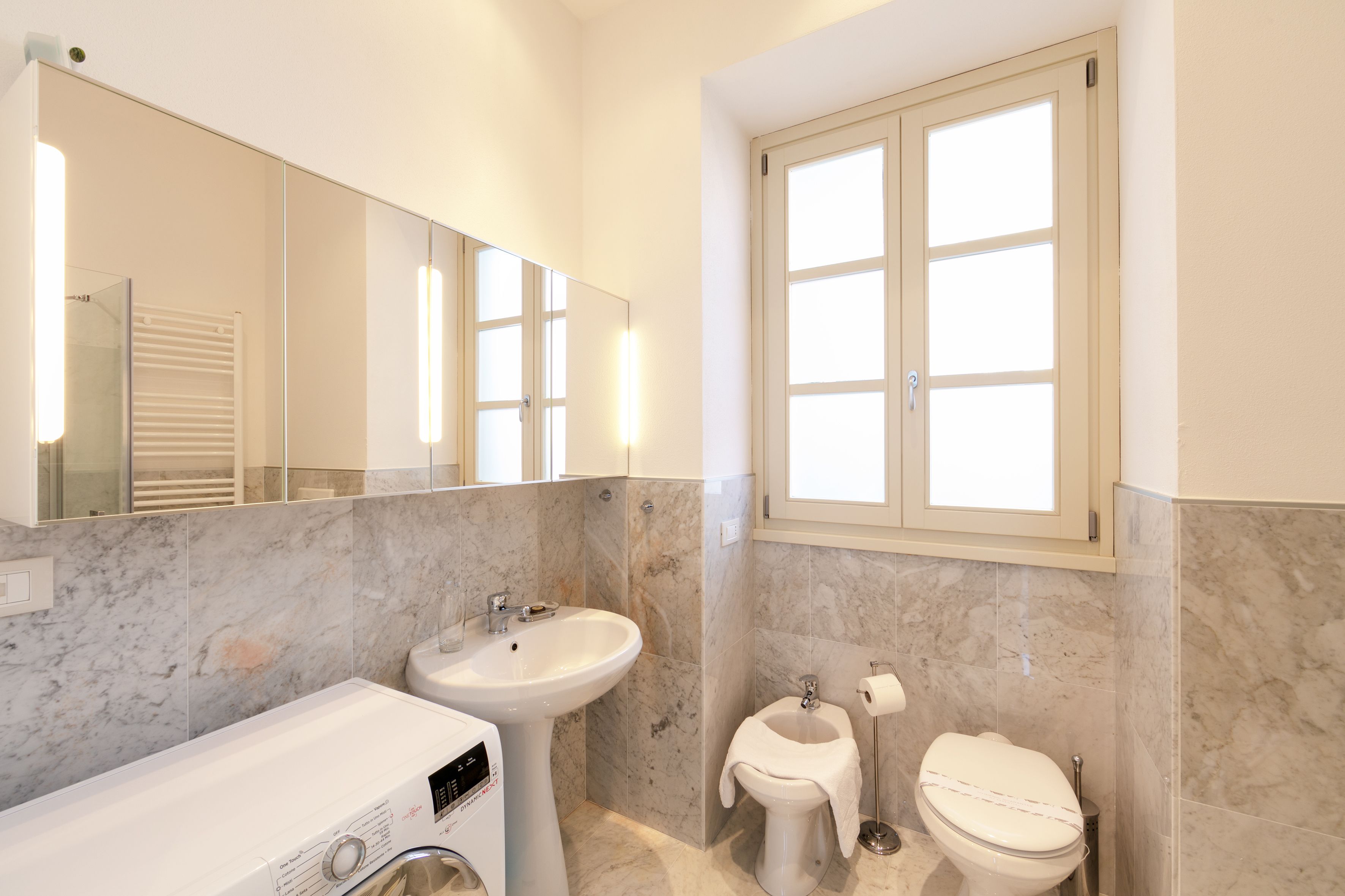 A modern bathroom with a built-in washing machine, a sink, and a toilet.