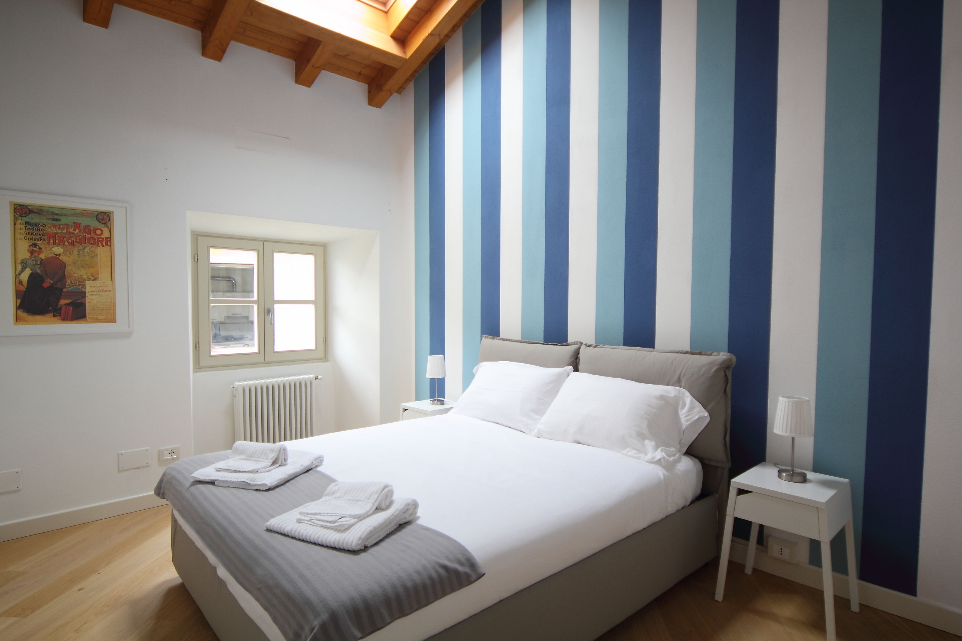 A bedroom with a large bed, white linens, a window, and a striped wall.