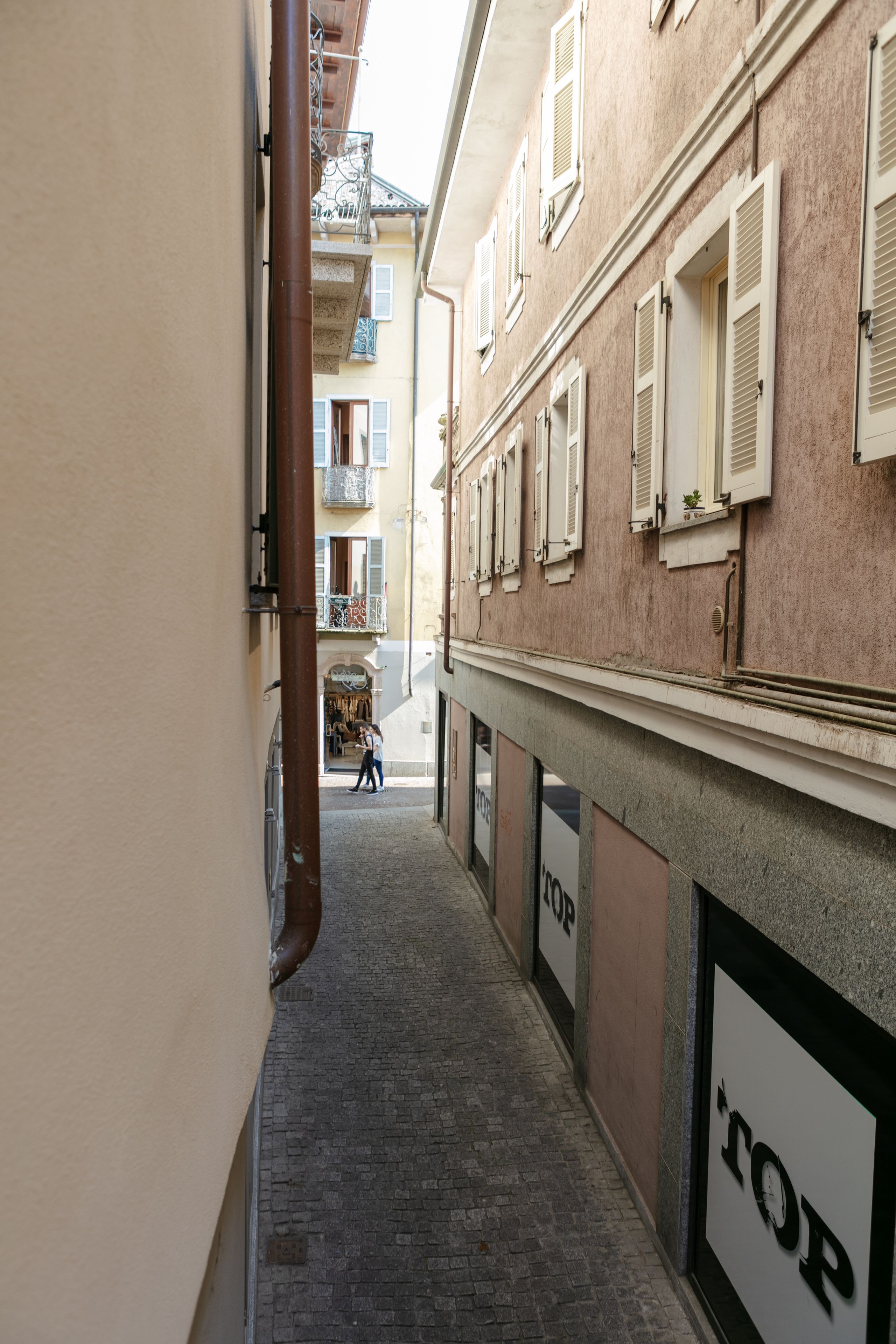 A narrow alleyway with buildings on either side, a person walking in the distance, and a 'TOP' sign on the right wall.
