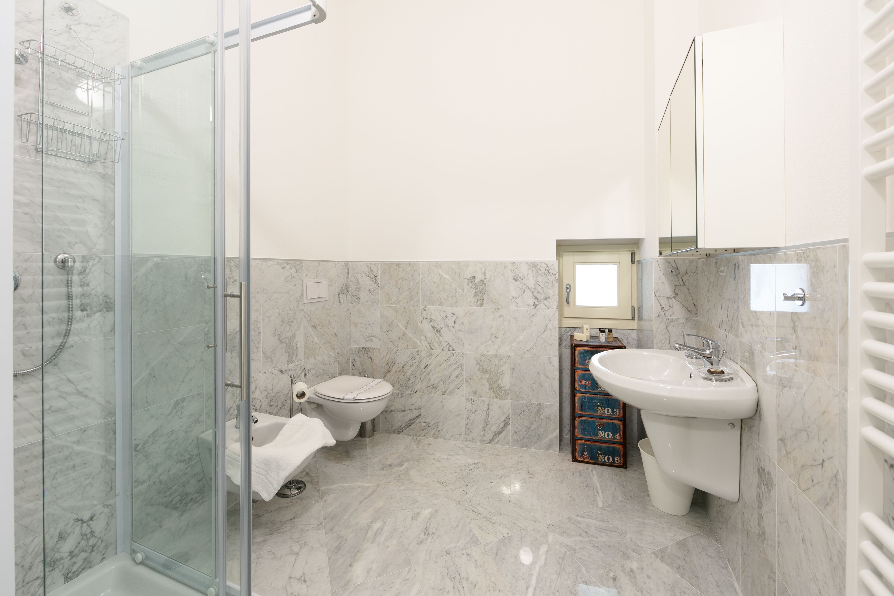 Un baño moderno con ducha de vidrio, inodoro y lavamanos con espejo arriba.