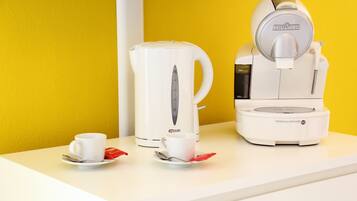 A coffee maker and a kettle on a white table against a yellow wall.