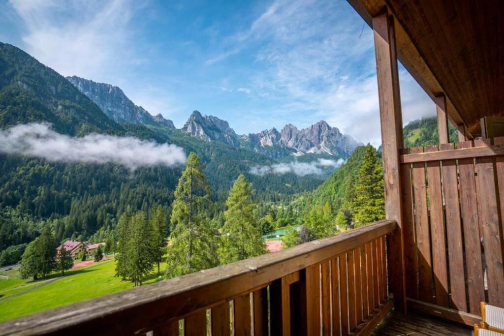 Un balcone in legno con vista su un paesaggio montuoso, che include una casa e una zona boschiva.