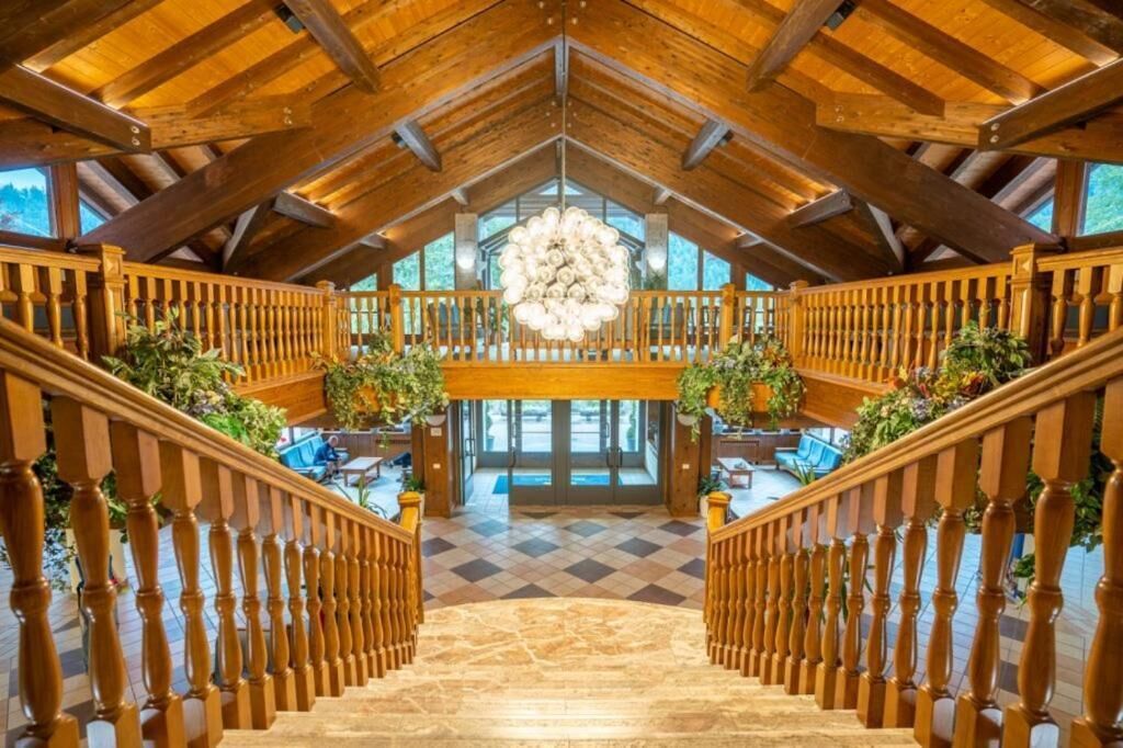 Un grand escalier en bois, avec des rampes, menant à un niveau supérieur, un lustre et un sol à carreaux.