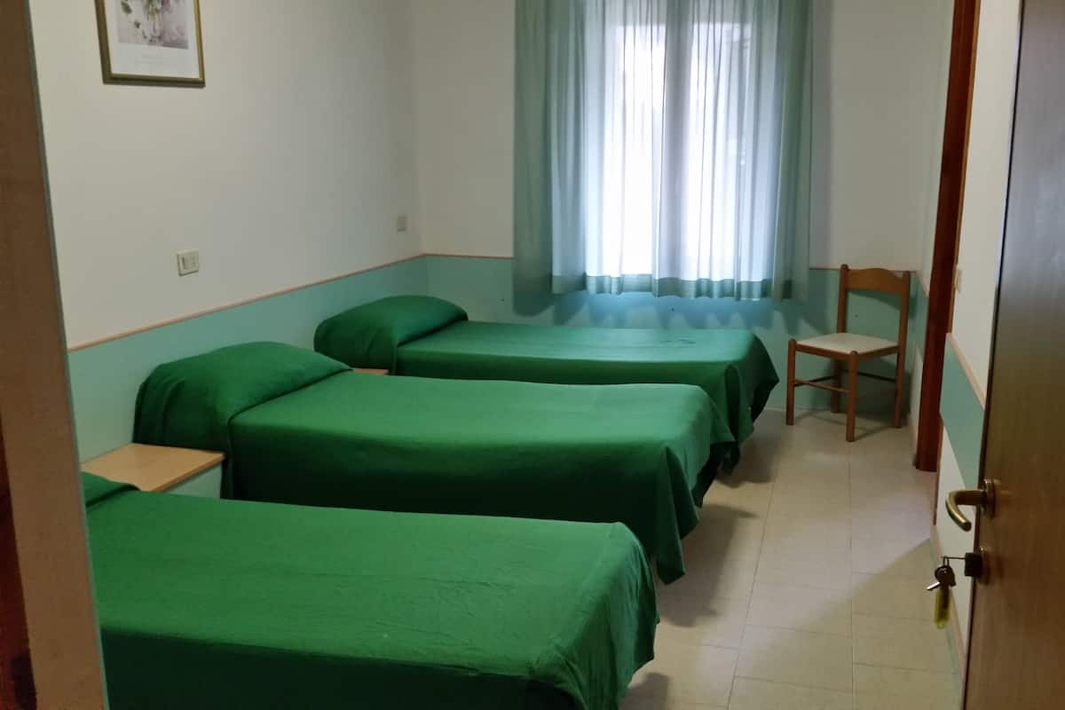 A room with three single beds, a wooden chair, and a door.