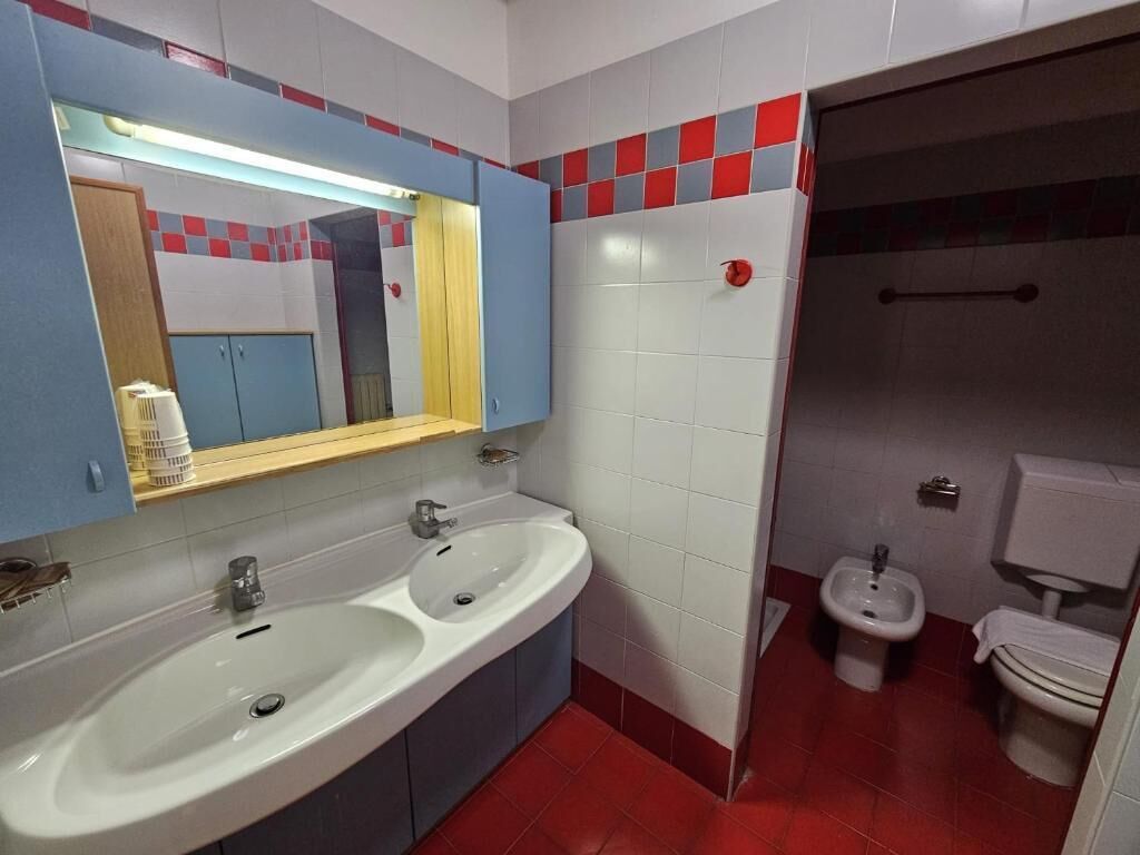 A bathroom with two sinks, a mirror, a toilet, and a bidet.
