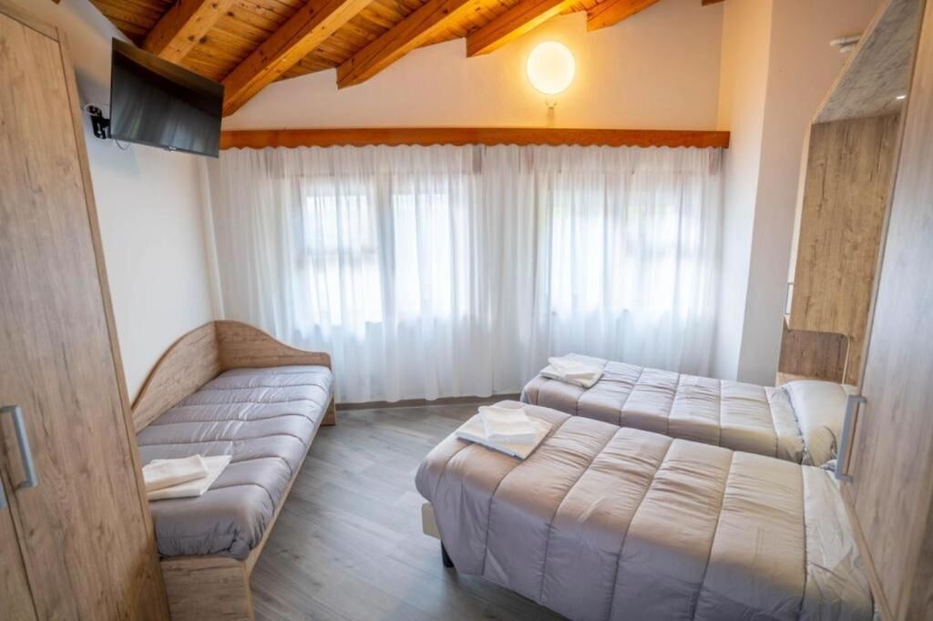 A room with two beds, wooden beams on the ceiling, a TV mounted on the wall, and a window with curtains.