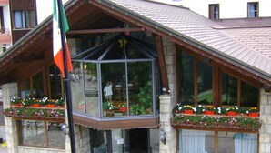 A building with a glass entrance, wooden balconies with flower boxes, and a flag.